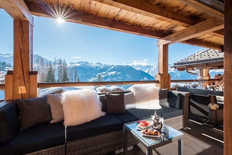 Covered chalet terrace with sofas, looking out over snow-capped mountains