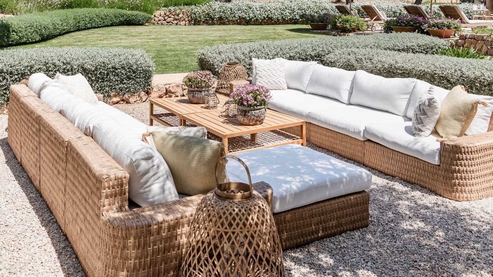 Wicker sofas and a teak table on a gravel terrace, with clipped hedges and a lawn behind